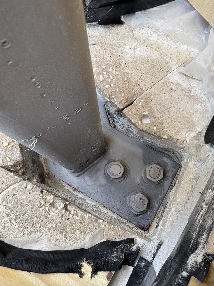 Close-up of a bolted steel column base plate anchored to a concrete slab